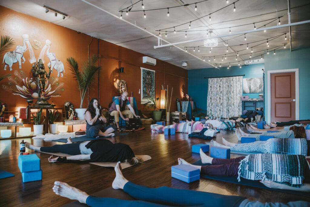 Students resting in savasana with live music in the main studio at Karma Yoga Center
