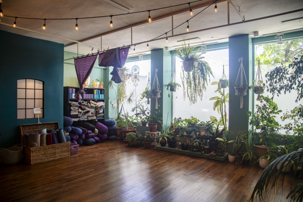 Sunlit main studio with plants, props, and string lights at Karma Yoga Center