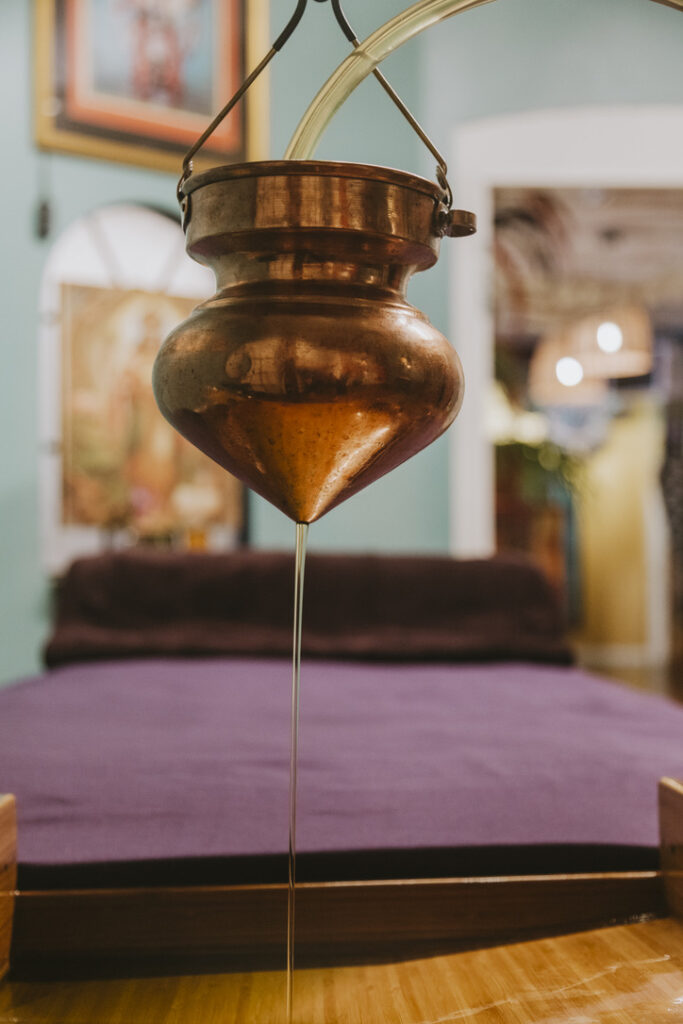 Warm oil flowing from a copper Shirodhara vessel at the Soma Spa, Denver