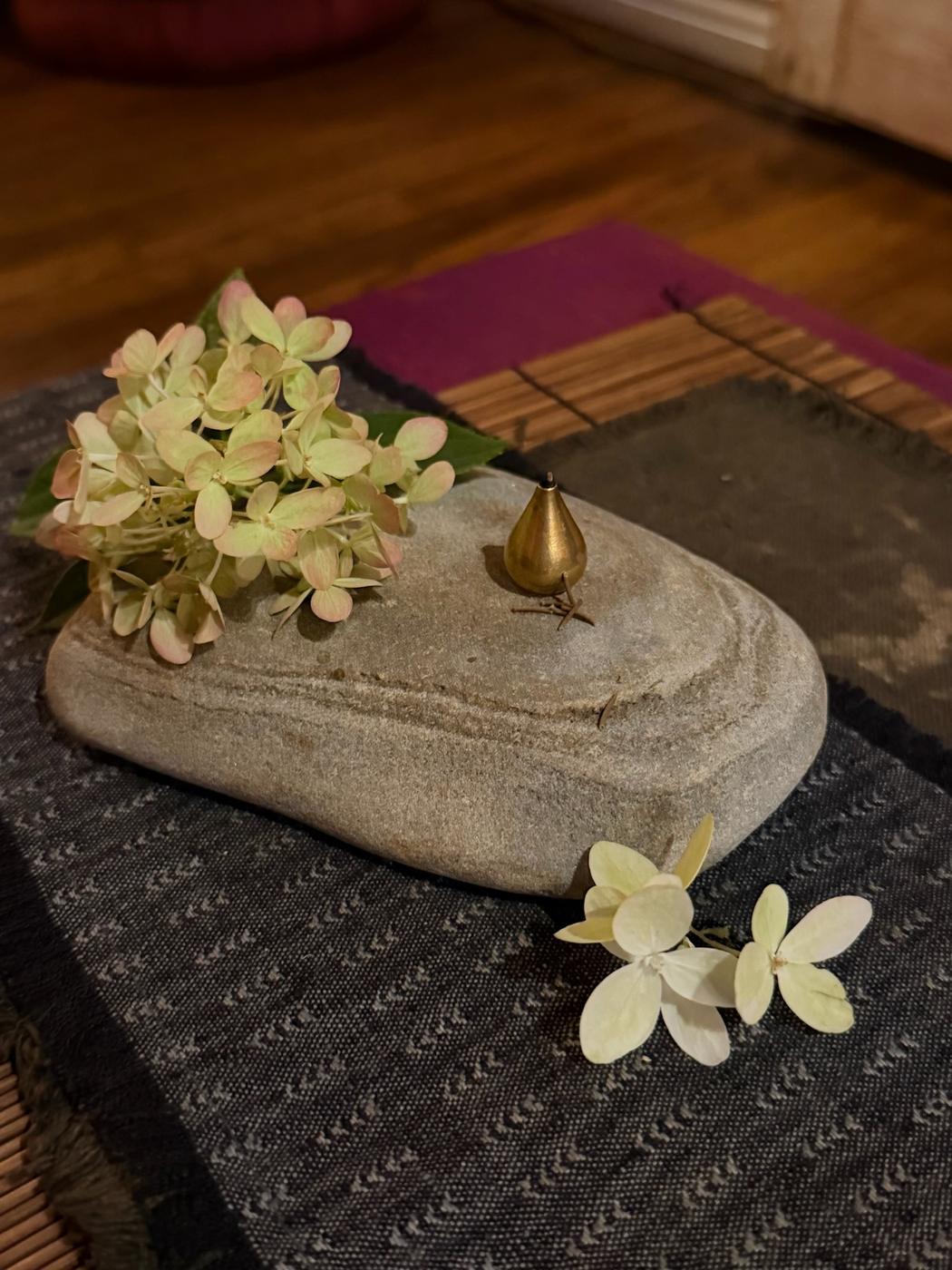 Hydrangea blossoms and a brass incense holder on a river stone at the tea table